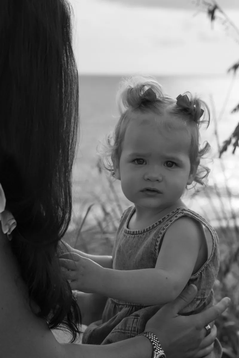 Black and white portrait of a toddler held by her mother beside the sea oats