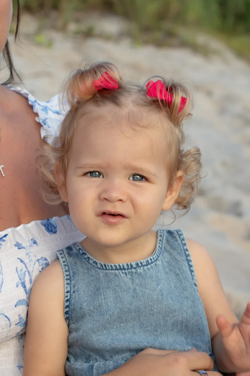 Close portrait of a curly haired toddler with pink bows in her pigtails