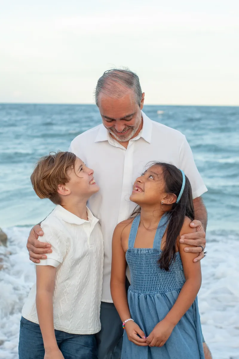 Father hugging his son and daughter in the surf as the kids smile up at him