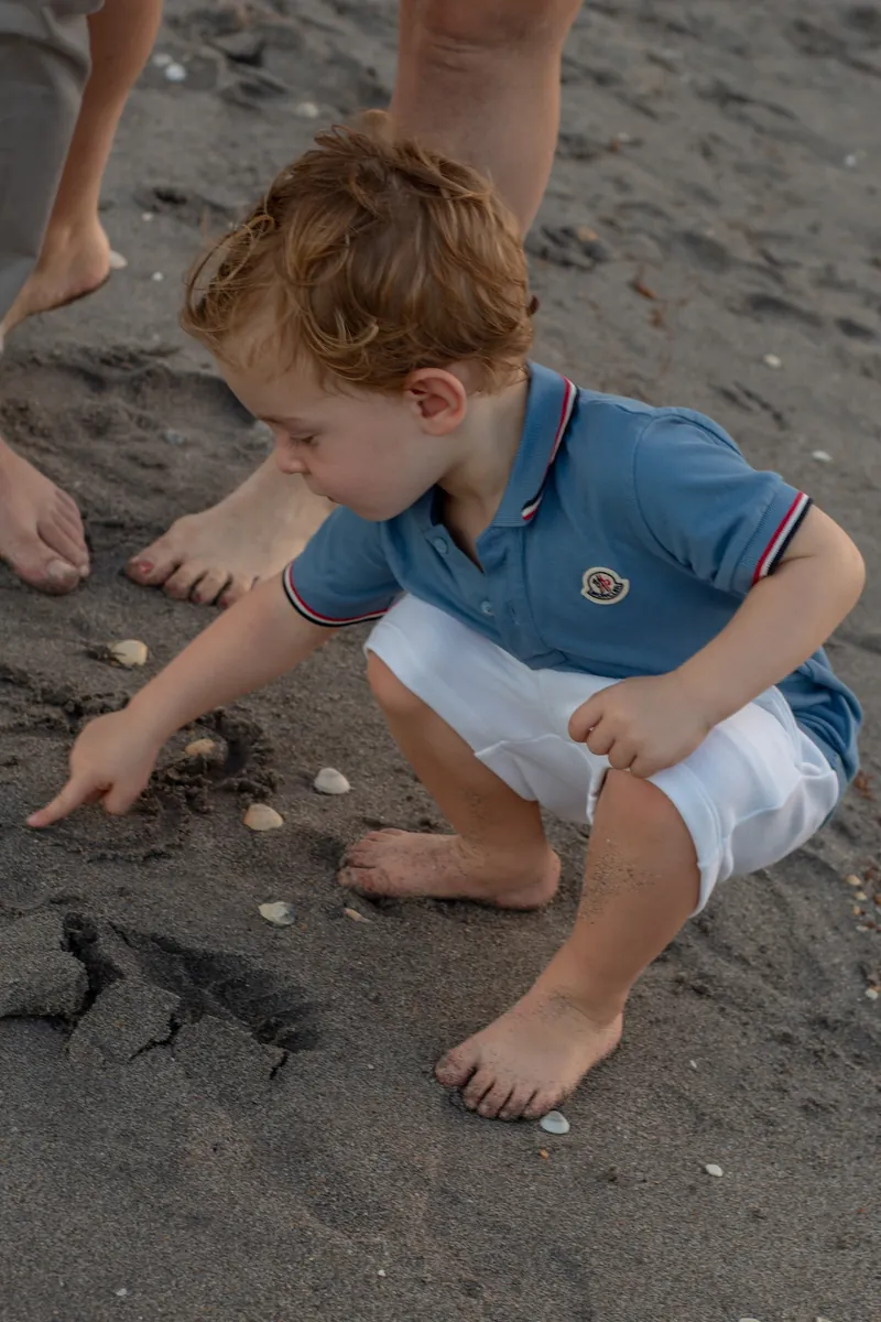 Little boy in a blue polo crouching to draw in the sand on a Jupiter beach