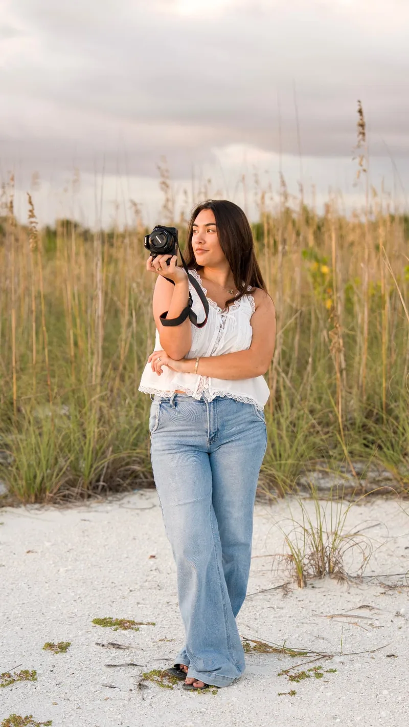 Abbi McLain, photographer at Kavanah Photography, holding her camera among the sea oats on a Florida beach