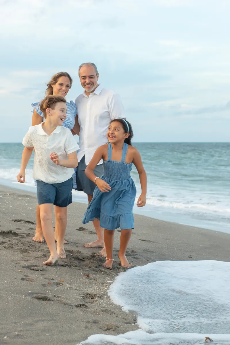 Family of four walking barefoot along the shoreline on a Jupiter, Florida beach