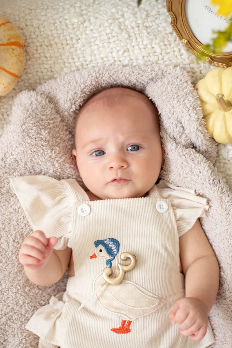 Newborn baby in a cream romper lying on a soft knit blanket during a lifestyle session