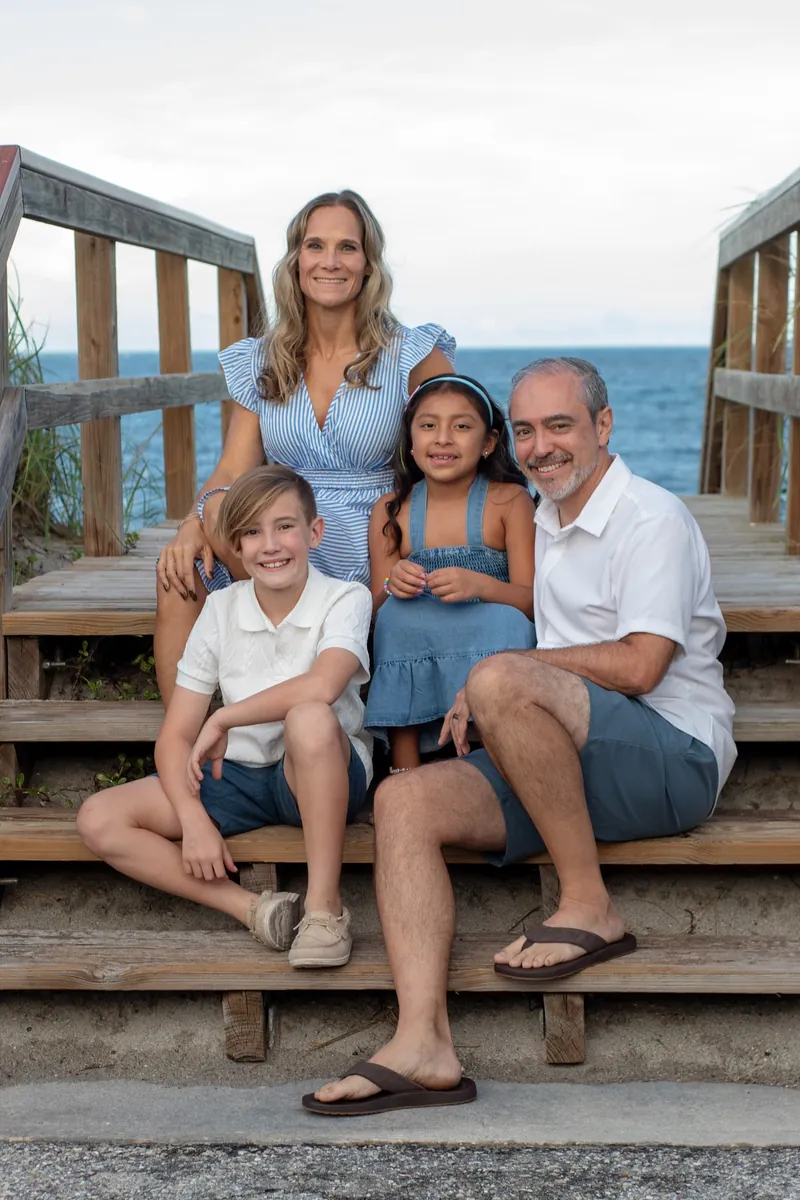 Family of four smiling together on wooden beach access steps with the ocean behind them in Jupiter, Florida